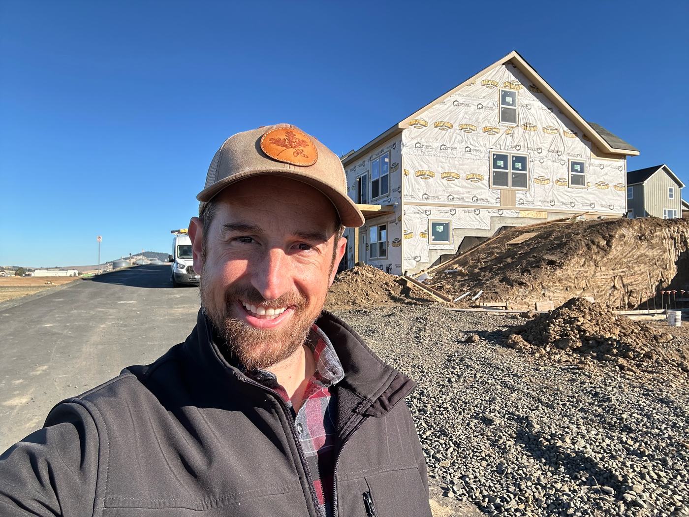 Charlton Haupt smiling in front of a house under construction, wrapped and sitting above a gravel slope.