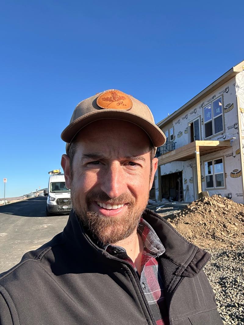 Charlton Haupt smiling, a work van on the road behind him and a house under construction to the side.